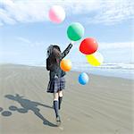 Young Japanese woman in a high school uniform running with balloons by the sea, Chiba, Japan