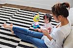 Woman with baby daughter sitting on floor using smartphone touchscreen