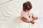 Overhead view of baby girl sitting up on bed