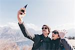 Couple taking smartphone selfie above mountain lakeside, Monte San Primo, Italy