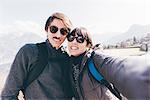 Couple taking smartphone selfie above mountain lakeside, Monte San Primo, Italy