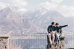 Couple sitting on terrace wall over mountain lakeside, Monte San Primo, Italy