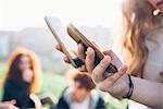 Two young women outdoors, looking at smartphones, mid section, close-up