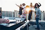 Group of friends enjoying roof party, young man using mixing desk