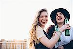 Two young women, outdoors, drinking bottled beer, laughing