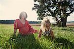 Pregnant woman sitting in field with toddler daughter crawling in grass