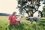 Pregnant woman sitting in field with toddler daughter playing with dog