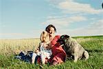 Pregnant woman sitting in field with toddler daughter and dog