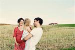 Pregnant couple in wheat field with toddler daughter