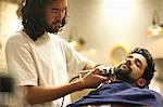 Hairdresser in barbershop shaving customer's beard