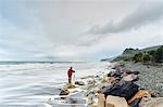 Tourist at edge of sea, Rapahoe, New Zealand