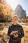 Portrait of woman holding camera in autumn landscape, Yosemite National Park, California, USA