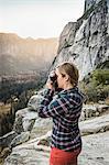Woman photographing landscape from rock formation, Yosemite National Park, California, USA