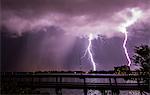 Double bolt of lightning strikes next to a rain shaft over Merritt Island, viewed from the State Road 520 Causeway bridge over Indian River Lagoon, Florida