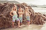 Portrait of three young sisters on beside rock on beach, smiling