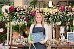 Portrait of florist in flower shop, holding 'open' sign