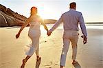 Mature couple walking along beach, hand in hand, rear view, Cape Town, South Africa