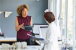 Female architect explaining virtual reality headset to colleague at office desk