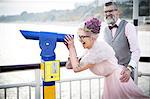 1950's vintage style couple looking through coin operated binoculars on pier