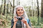 Mature woman with long grey hair photographing in forest, Scandicci, Tuscany, Italy