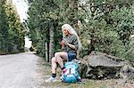 Mature female backpacker looking at smartphone on forest road, Scandicci, Tuscany, Italy