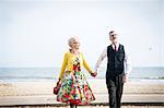 1950's vintage style couple holding hands and strolling on beach