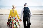 Rear view of 1950's vintage style couple holding hands and strolling on beach