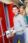 Teenage boy standing by red locker