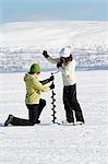 Women drilling hole in ice
