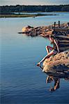 Teenage girl sitting on rock by lake