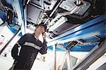 Female mechanic talking on mobile phone under a car