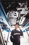 Female mechanic talking on mobile phone under a car