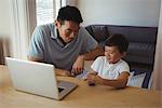 Father and son using mobile phone and laptop in living room