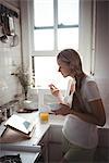 Woman having breakfast while looking at digital tablet in kitchen