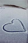 Heart shape drawn on car bonnet covered with snow