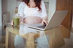 Mid section of pregnant woman using laptop while having juice