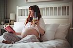 Pregnant woman having juice while reading book on bed