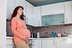 Thoughtful pregnant woman standing in kitchen