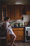 Woman using mobile phone while having coffee in kitchen