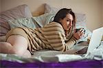 Woman using laptop while having coffee on bed