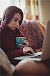 Woman having coffee while using laptop on sofa
