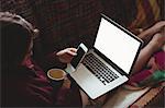 Woman having coffee while using laptop and mobile phone on sofa