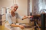 Portrait of female worker pouring honey from storage tank at apiary