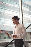 Businesswoman looking at digital tablet while walking by glass window