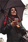 Low angle view of woman looking away while holding mobile phone and umbrella