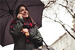 Low angle view of woman talking on mobile phone while holding umbrella