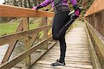 Mid section of woman performing stretching exercise on the bridge in forest