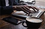 Mid section of man using laptop while having coffee in Café