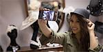 Woman taking selfie while trying hat in jewelry section of boutique