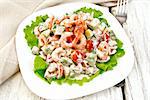 Salad with shrimp, avocado, tomatoes and mayonnaise on the green lettuce in a plate, napkin, fork on the background light wooden boards